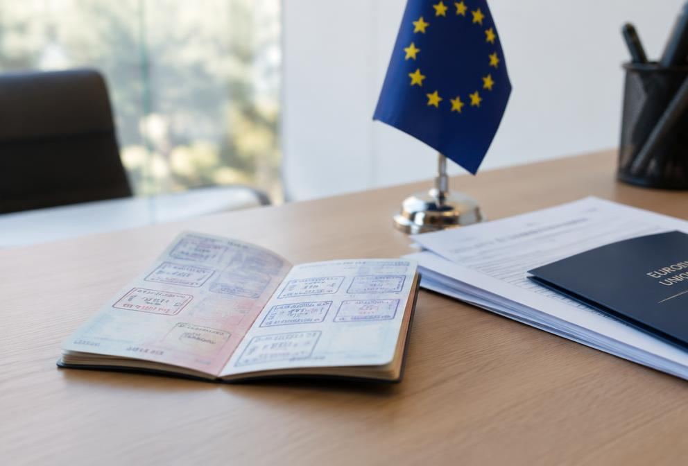 A passport with visa stamps beside an EU flag on an immigration office desk