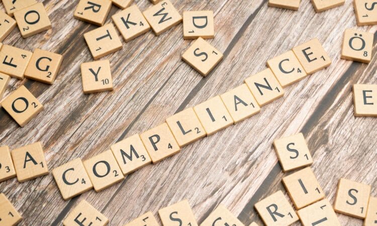Wooden letter tiles forming the word 'COMPLIANCE' on a rustic wooden background.