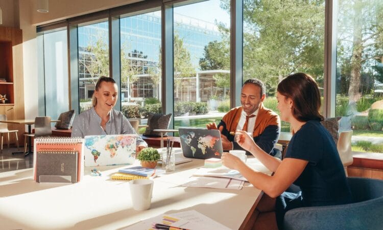 Three colleagues brainstorming with laptops in a well-lit office.