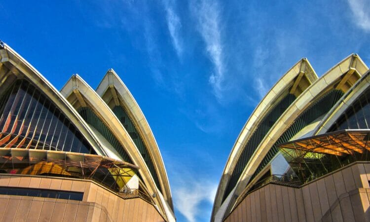 A striking low angle view of the iconic Sydney Opera House with a vibrant blue sky background, showcasing its modern architectural design.