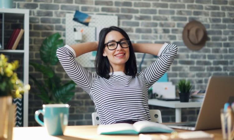 a woman sitting at a desk with her hands behind her head