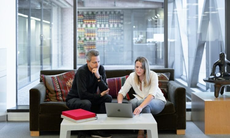 man and woman sitting on couch using macbook