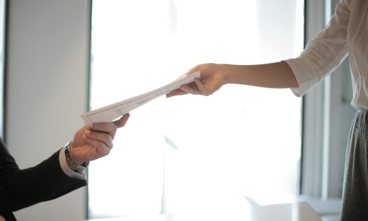 Close-up of hands exchanging documents in a business setting indoors.