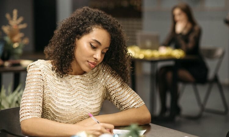 Young woman writing in a festive indoor office with a blurred background and glittery attire.