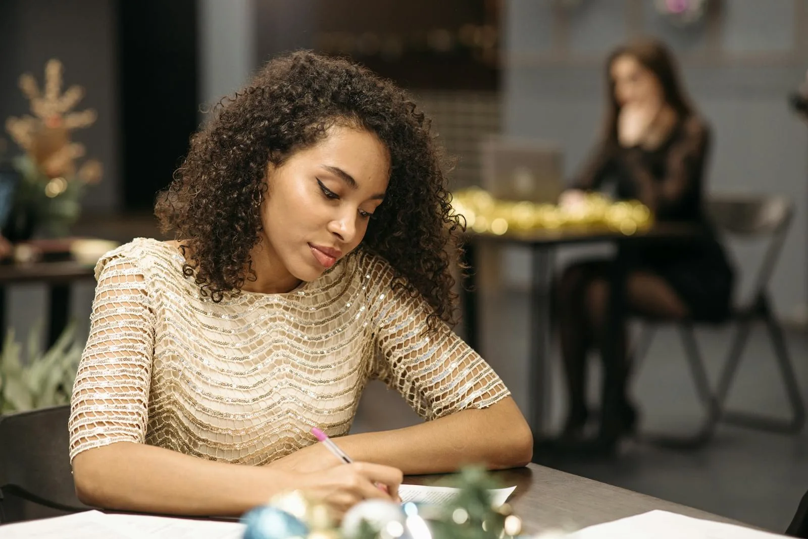 Young woman writing in a festive indoor office with a blurred background and glittery attire.