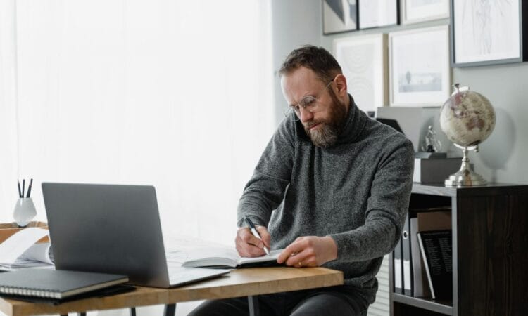 Man concentrating on work at home office desk with laptop and documents.