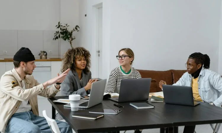 Group of diverse colleagues collaborating with laptops in a modern office setting.