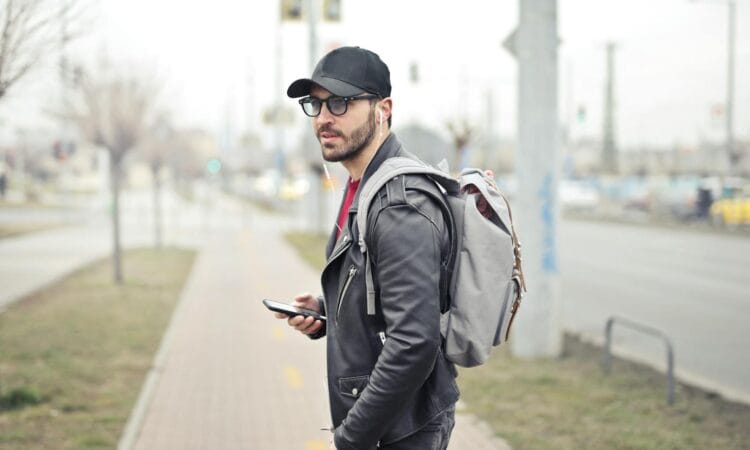 A fashionable young man in Budapest checking his smartphone on a busy street.