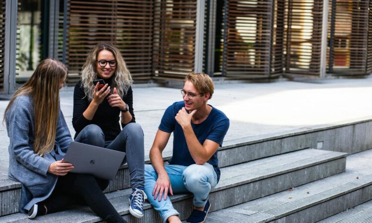 Three young professionals having a friendly chat while sitting on outdoor steps.