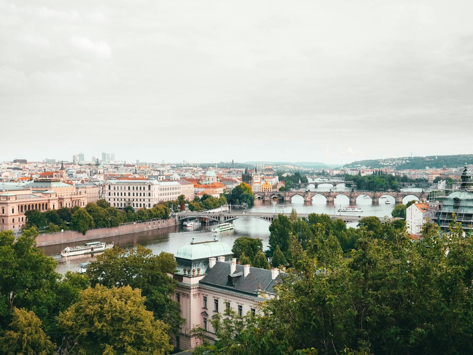 Discover the charming cityscape of Prague with its iconic bridges spanning the Vltava River, framed by lush greenery.