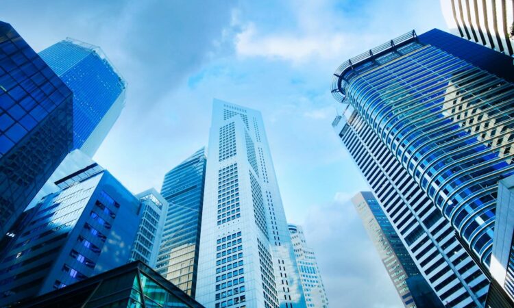 A breathtaking low angle view of modern skyscrapers with glass and concrete facades under a blue sky.