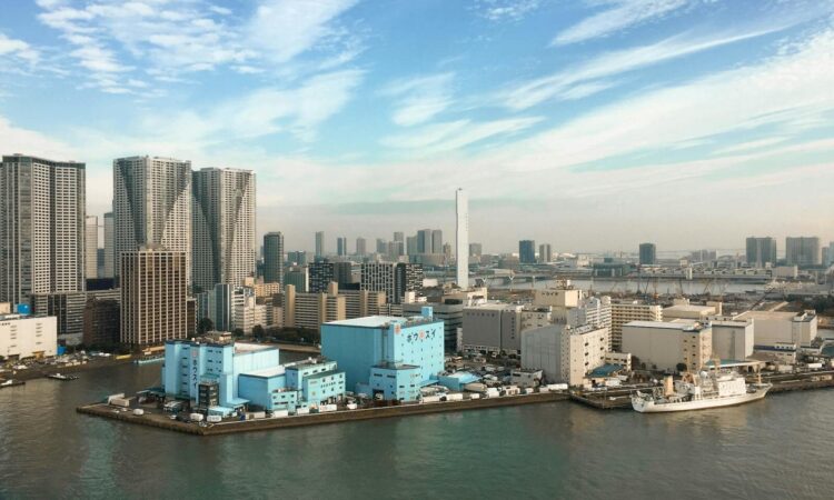 Aerial view of a modern city skyline with skyscrapers and waterfront buildings under a clear blue sky.