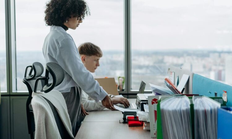 Two coworkers collaborate in a modern office with a city view, enhancing teamwork and productivity.